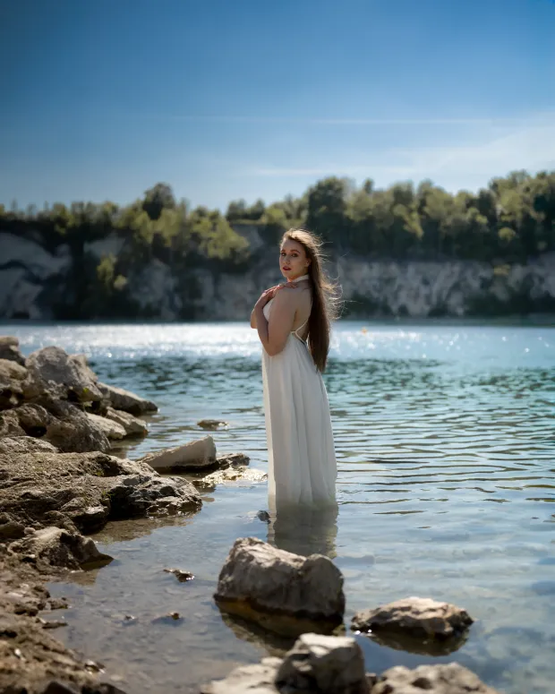 Woman in a white dress by the water, among stones